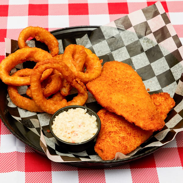 Fried fish fillets, onion rings, and coleslaw in a black basket on a red and white checkered tablecloth.