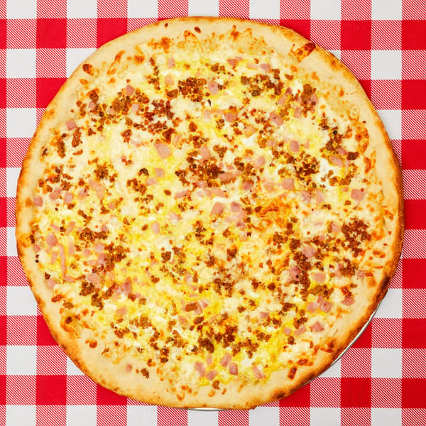 A whole meat-topped pizza with a golden crust on a red and white checkered tablecloth.