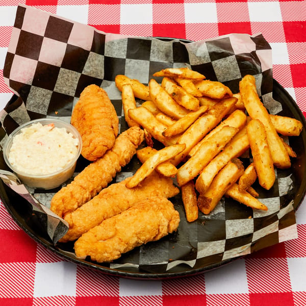 Fried fish and french fries with coleslaw in a black basket on a red and white checkered tablecloth.