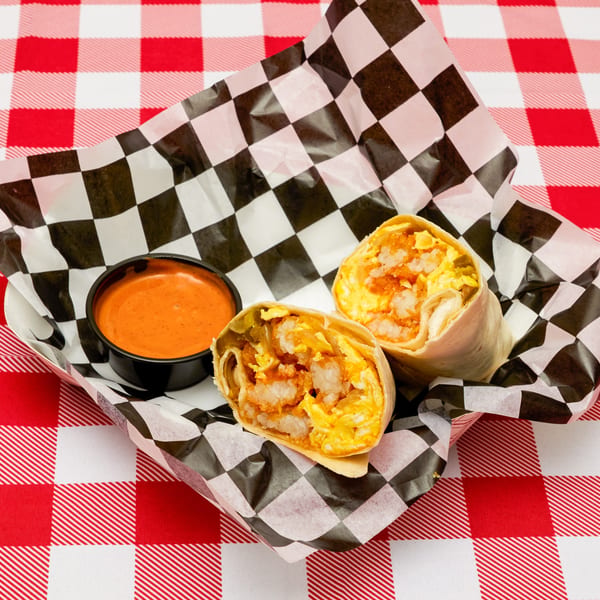 Two breakfast burritos with shrimp, eggs, and hash browns, served with a side of sauce.