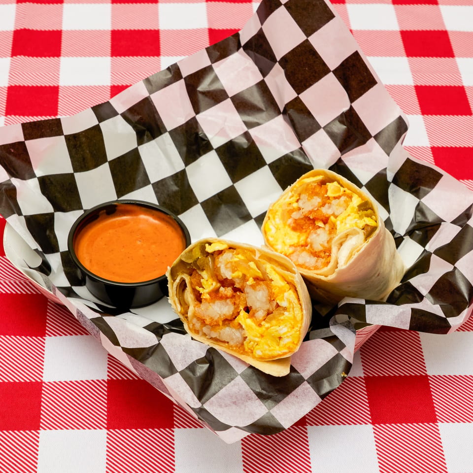 Two breakfast burritos with shrimp, eggs, and hash browns, served with a side of sauce.