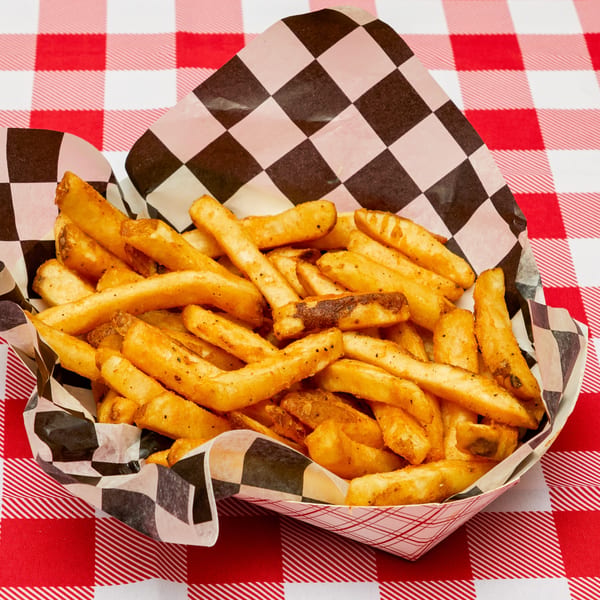 Seasoned french fries in a checkered paper tray on a red and white gingham tablecloth.