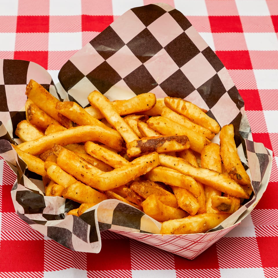 Seasoned french fries in a checkered paper tray on a red and white gingham tablecloth.