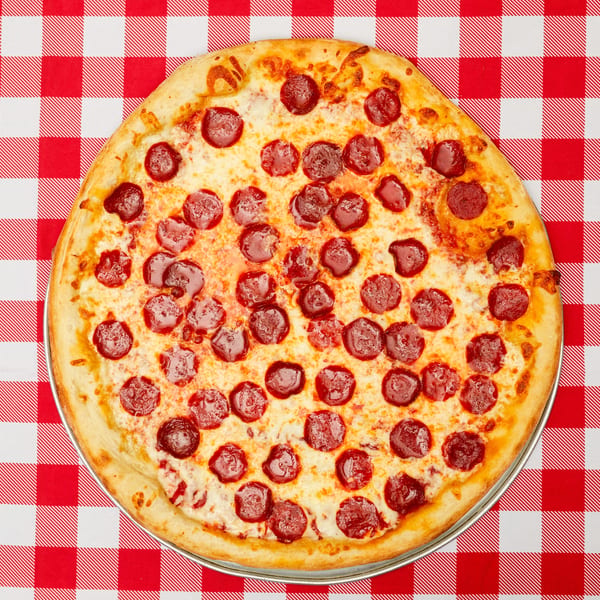 A whole pepperoni pizza on a metal tray, centered on a red and white checkered tablecloth.