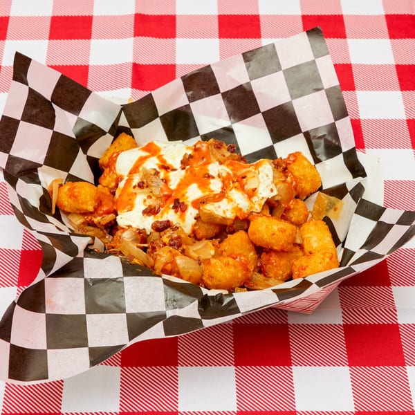 Loaded tater tots with cheese, bacon, onions, and hot sauce in a checkered paper tray.