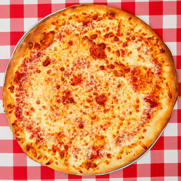 A large, cheesy pizza with a golden crust sits on a red and white checkered tablecloth.