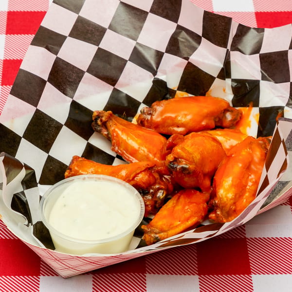Buffalo chicken wings with ranch dressing in a checkered paper tray on a red and white tablecloth.