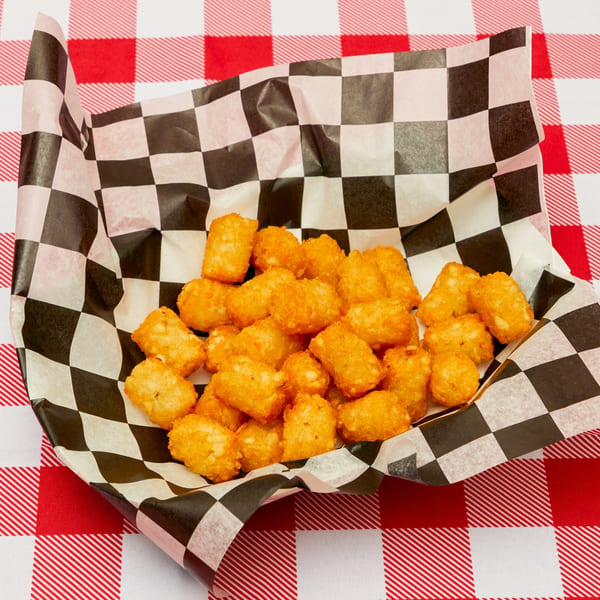 Golden-brown tater tots in a black and white checkered paper liner on a red and white checkered tablecloth.