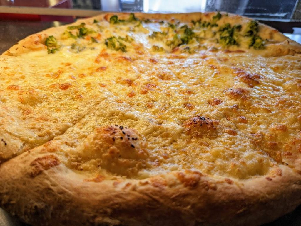 A pizza with cheese and broccoli.