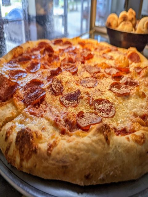 A pepperoni pizza sitting on a pan in front of a window.